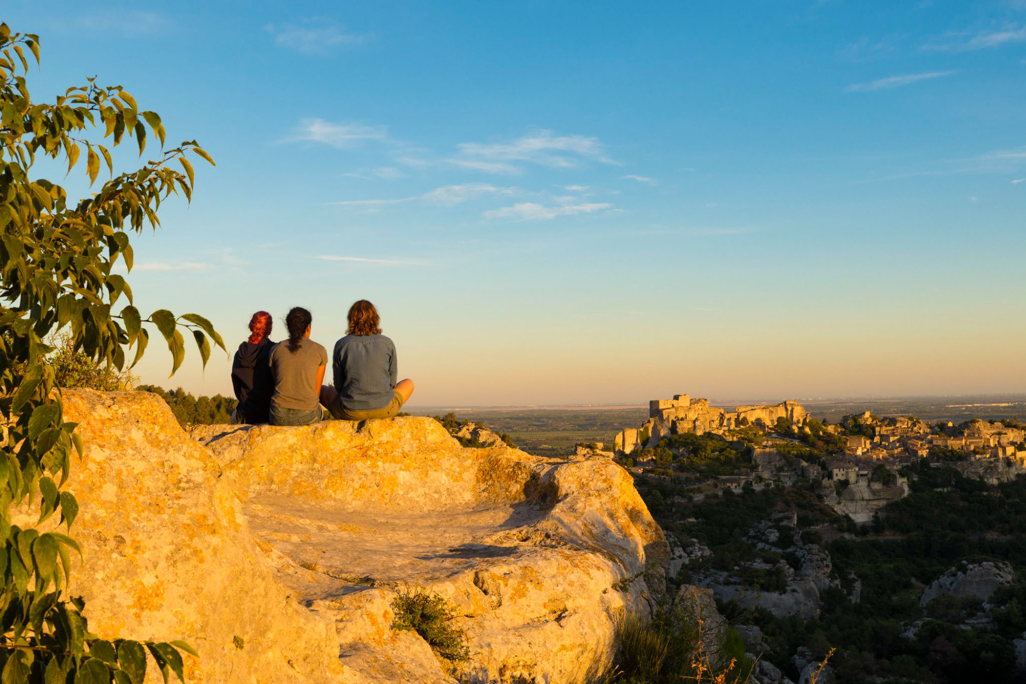 Deux personnes assises sur un rocher doré au coucher du soleil face aux Baux-de-Provence