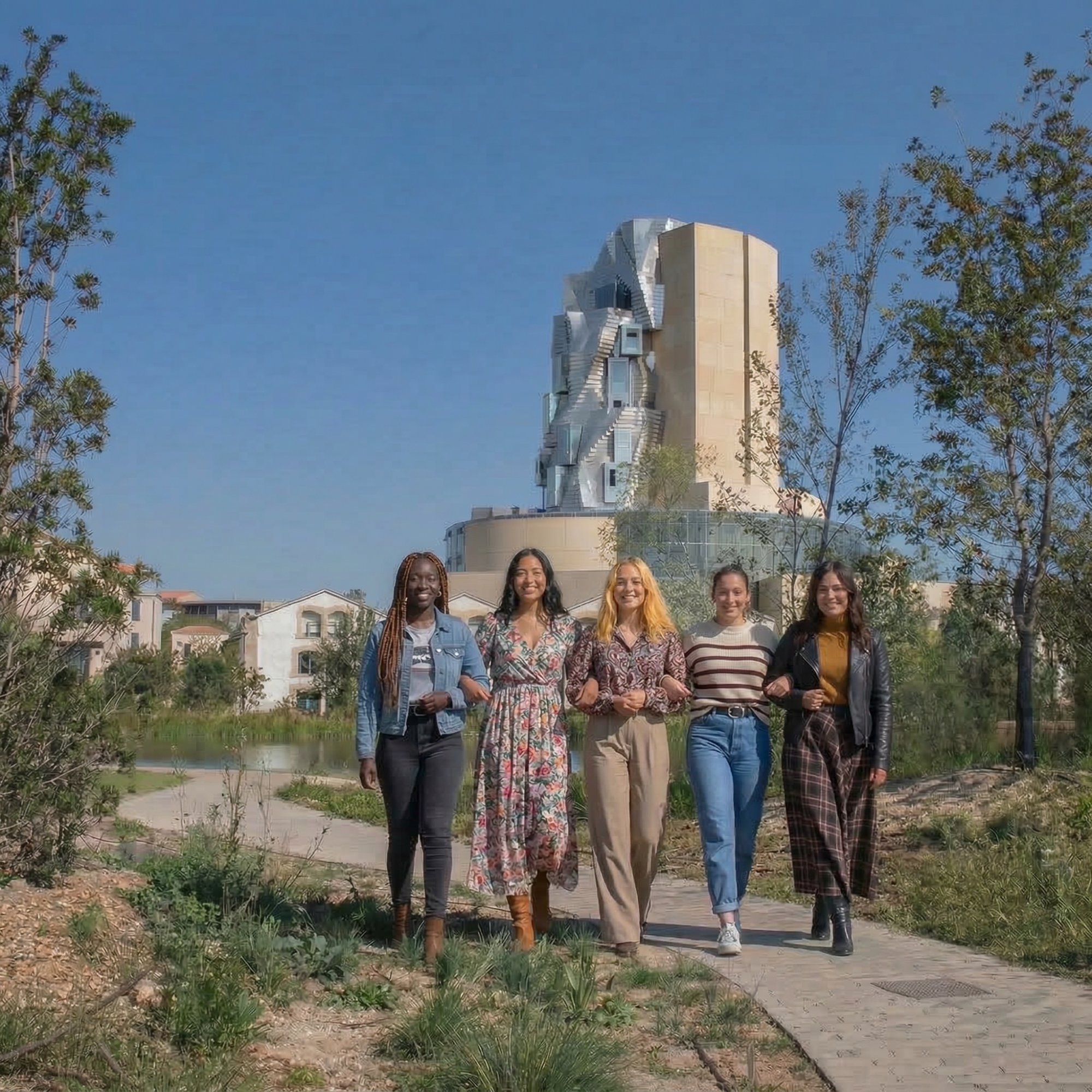 Groupe de femmes souriantes marchant dans le parc de la Fondation LUMA à Arles, tour Frank Gehry en arrière-plan