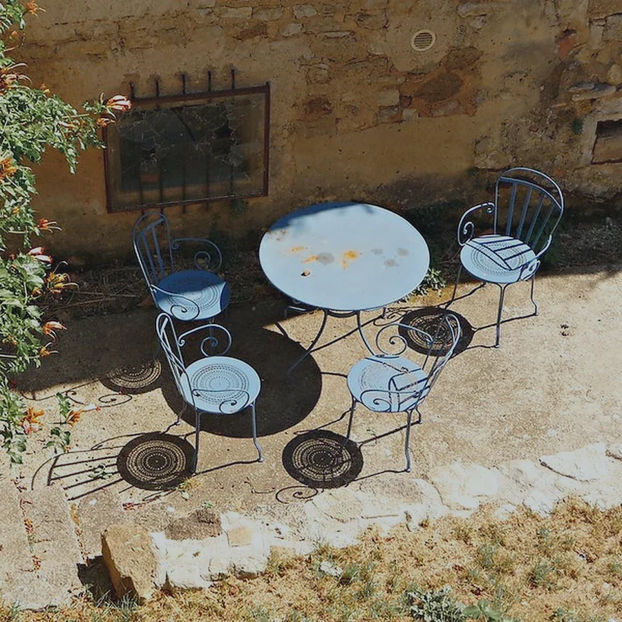 Table de bistrot bleue et chaises vides dans une cour, en plein soleil